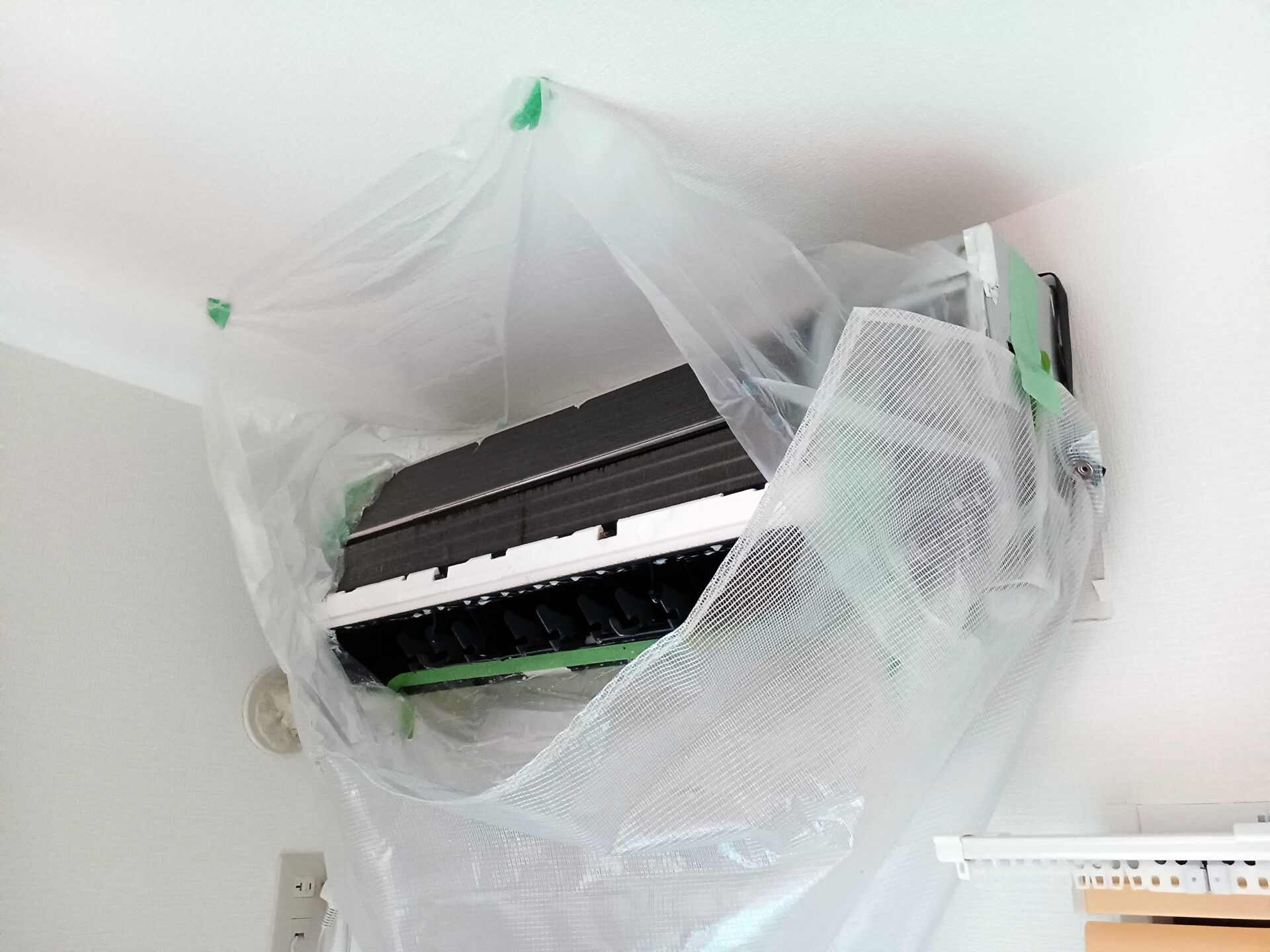 プロによるエアコンクリーニング。カバーを外し、周囲をビニールで養生している